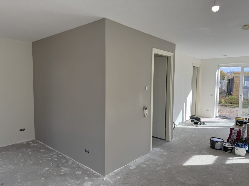 Renovlies behang dat net in een grijze kleur is geverfd, met verfemmers op de vloer